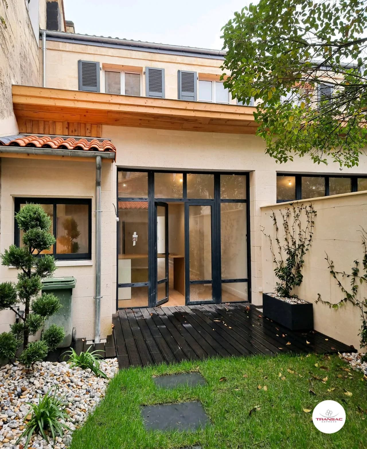 Jardin avec terrasse, maison moderne et baies vitrées.