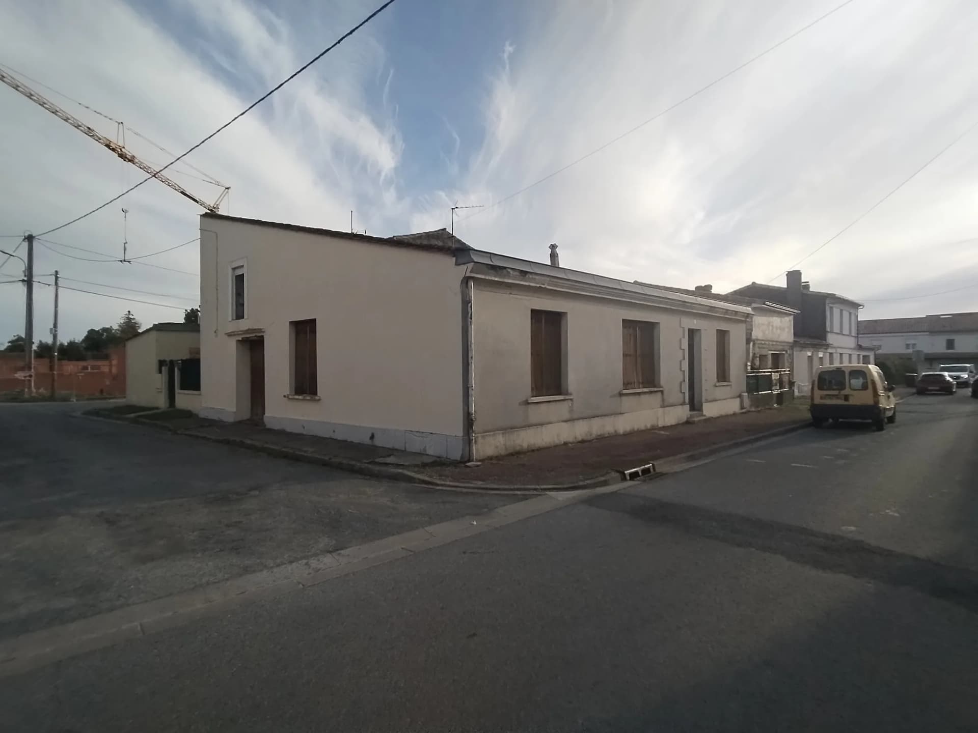 Maison de plain-pied avec fenêtres à volets, située au coin d'une rue.