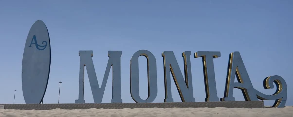 Panneau emblématique "MONTA" sur une plage ensoleillée.