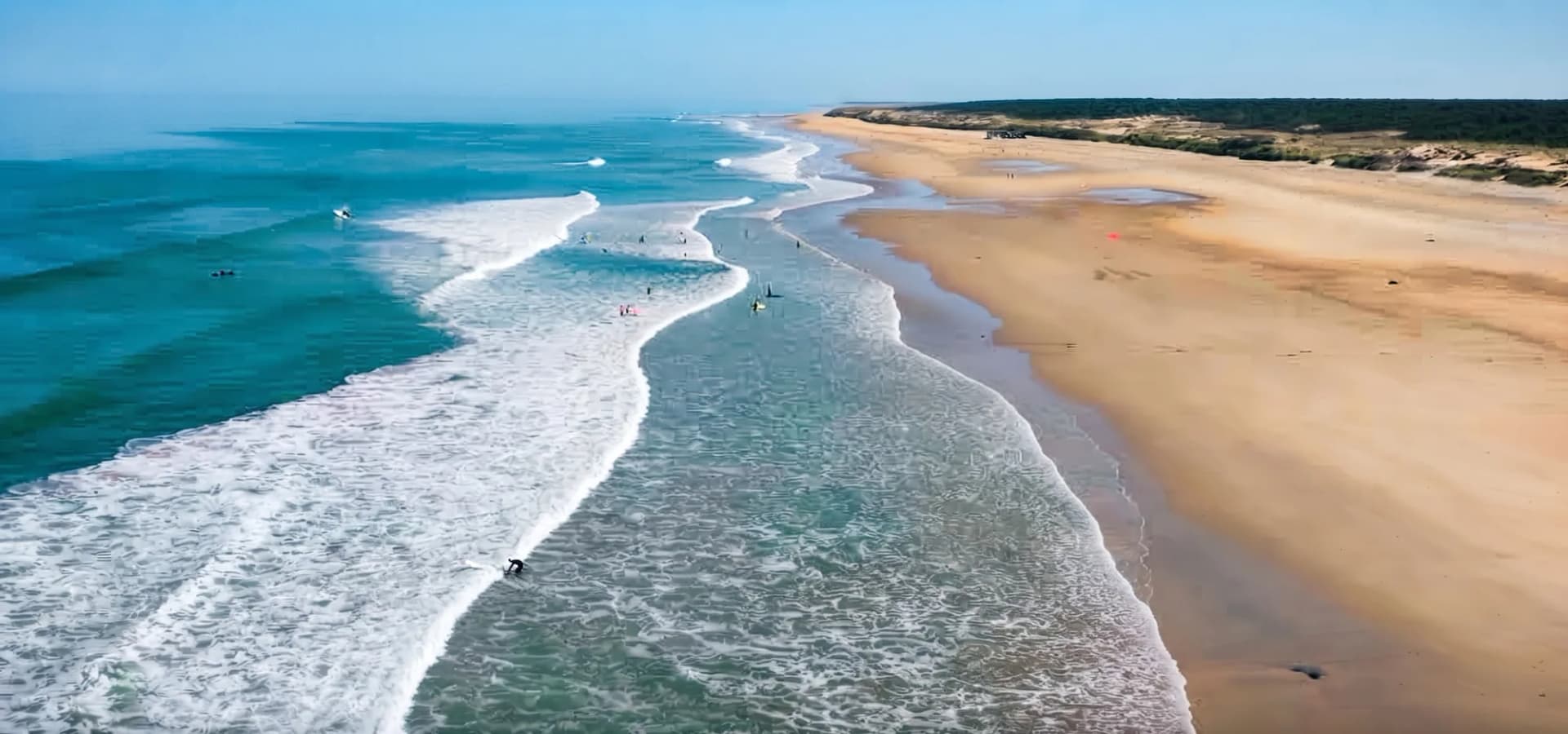 Plage tranquille avec vagues et surfers, ciel dégagé.