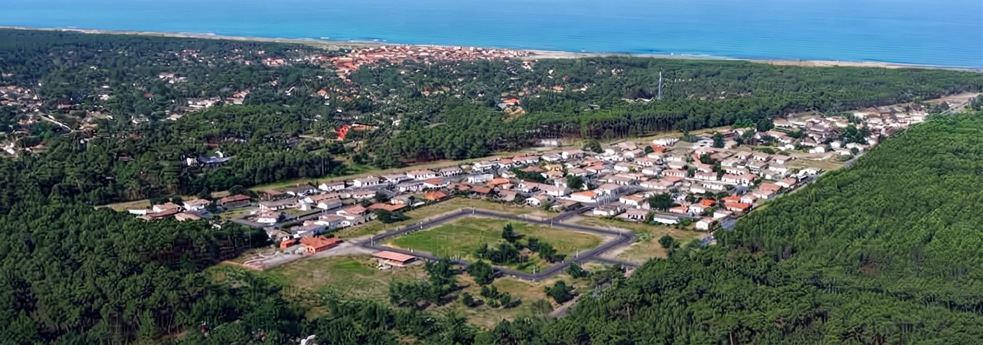 Vue aérienne d'un quartier résidentiel entouré de verdure et proche de la mer.