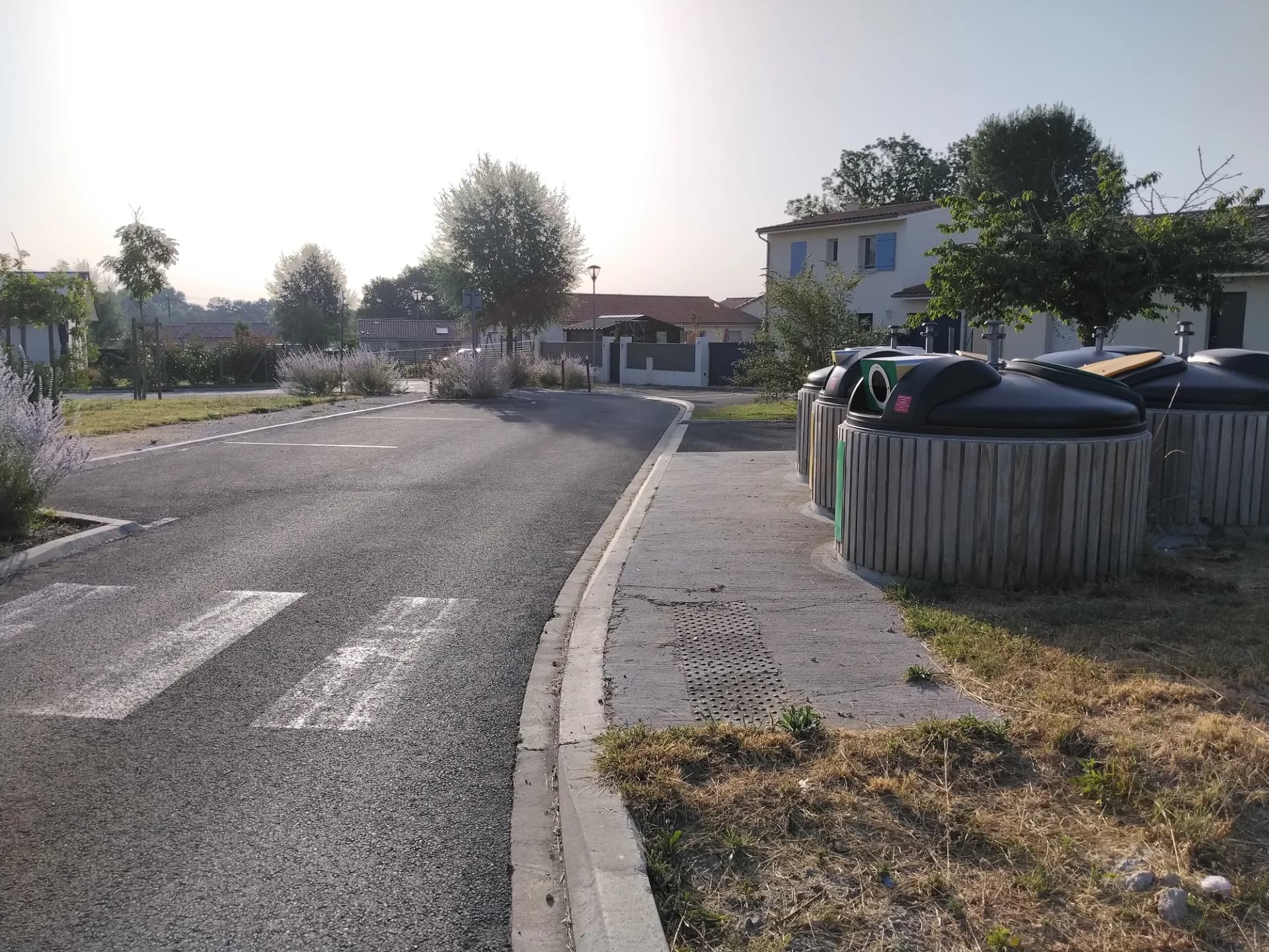 Vue d'une rue résidentielle avec des conteneurs de tri et espaces verts.