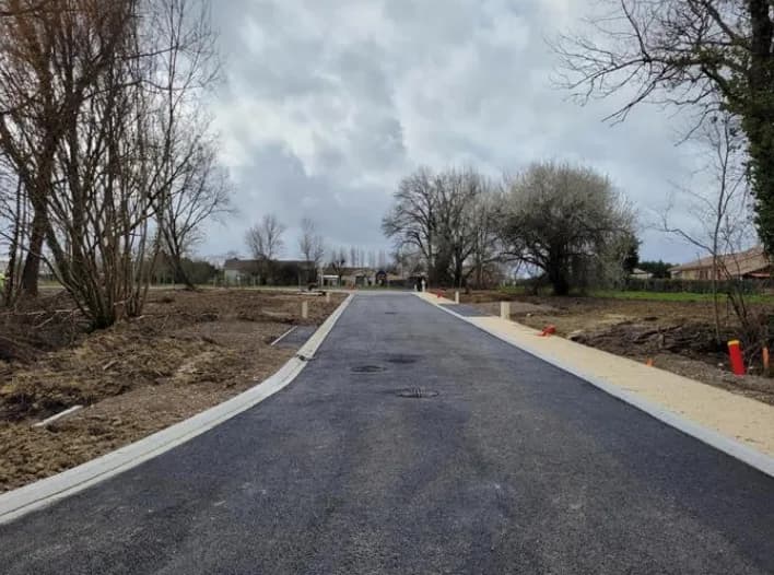 Allée en béton menant à un terrain dégagé avec arbres.